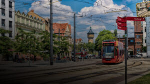 Rote Straßenbahn fährt durch eine Innenstadt mit historischen Gebäuden und Wegweisern. ©AdobeStock